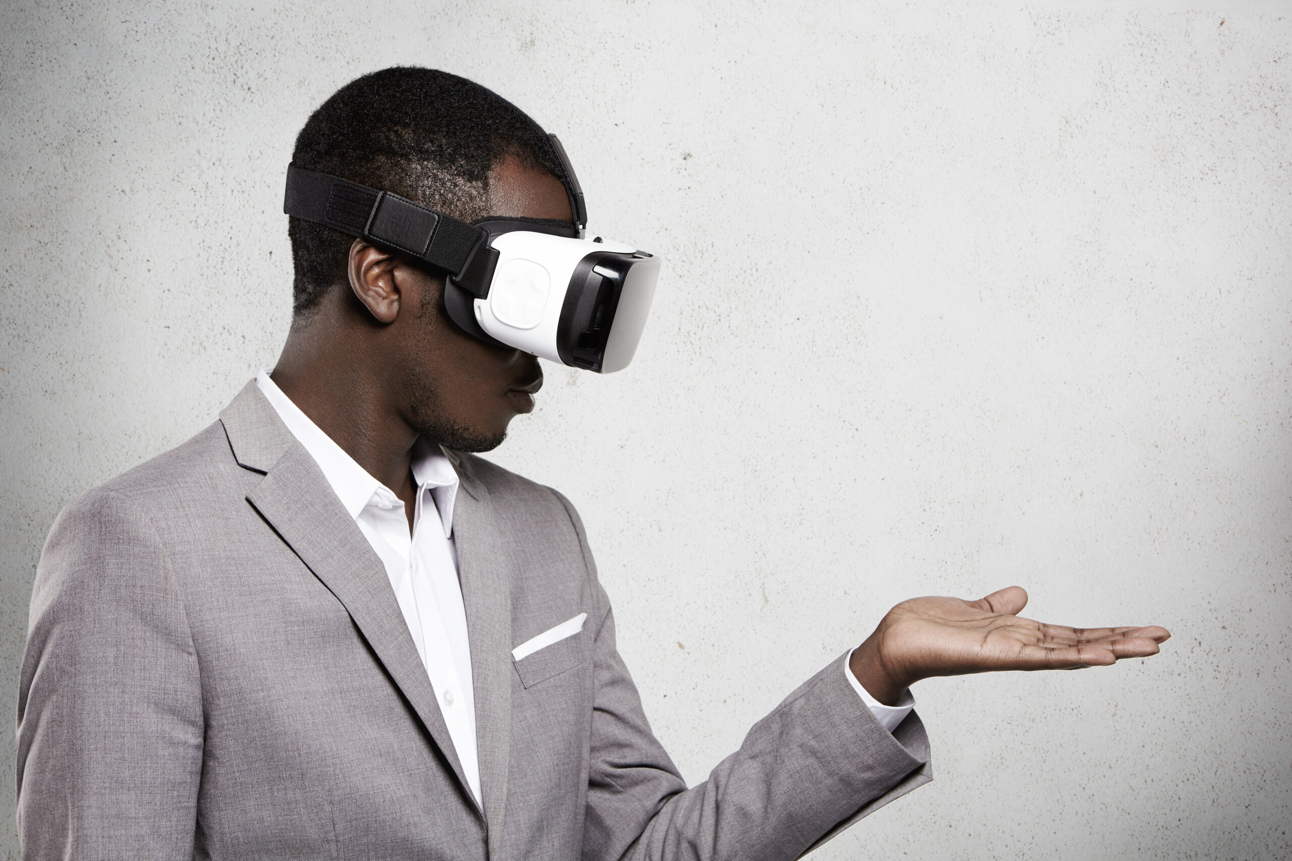 Technology, Entertainment, Gaming And Cyberspace. African Office Worker In Formal Suit Experiencing Virtual Reality Using 3d Headset For Mobile Phone, Looking At His Open Palm As If Holding Something