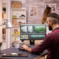 Back view of creative film maker working on a movie on laptop