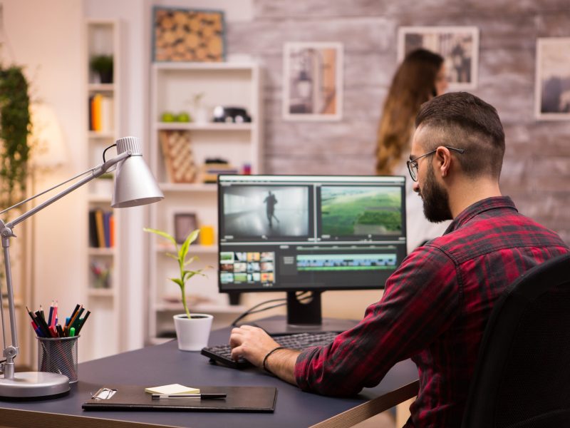 Back view of creative film maker working on a movie on laptop